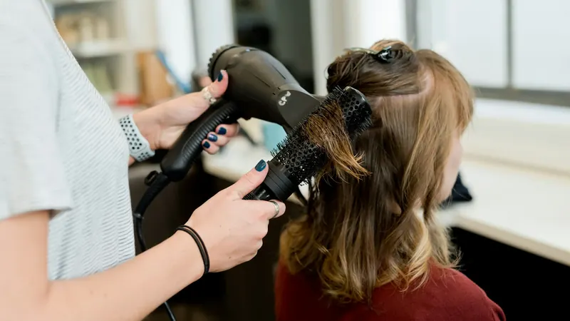 Friseurin föhnt die Haare einer Kundin mit Rundbürste